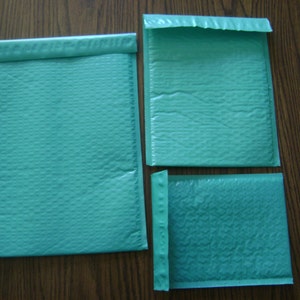 May include: Three teal blue padded envelopes of different sizes. The envelopes are made of a textured material and have a sealed flap.