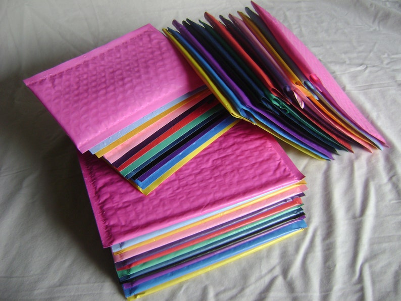 May include: A stack of colorful bubble mailers, with a pink mailer on top. The mailers are made of a textured, bubble-wrapped material.