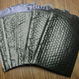 Könnte beinhalten: Ein Stapel von fünf schwarzen gepolsterten Versandtaschen mit einer Blasenstruktur. Die Umschläge sind gefaltet und bereit zum Versand.