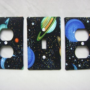 May include: Three black light switch covers with a space-themed design featuring planets, stars, and a galaxy background.
