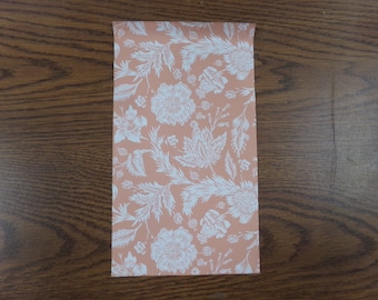 May include: A sheet of peach-colored wrapping paper with a white floral pattern. The pattern features stylized flowers, leaves, and stems.
