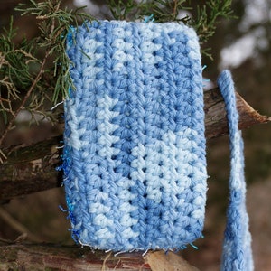 May include: A blue and white crocheted square with a sparkly blue trim. The square is hanging from a branch.