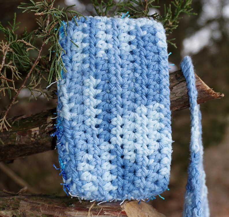 May include: A blue and white crocheted square with a sparkly blue trim. The square is hanging from a branch.