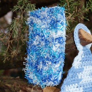 May include: A blue and white crocheted scarf with a fluffy texture. The scarf is made with a variety of shades of blue and white yarn.