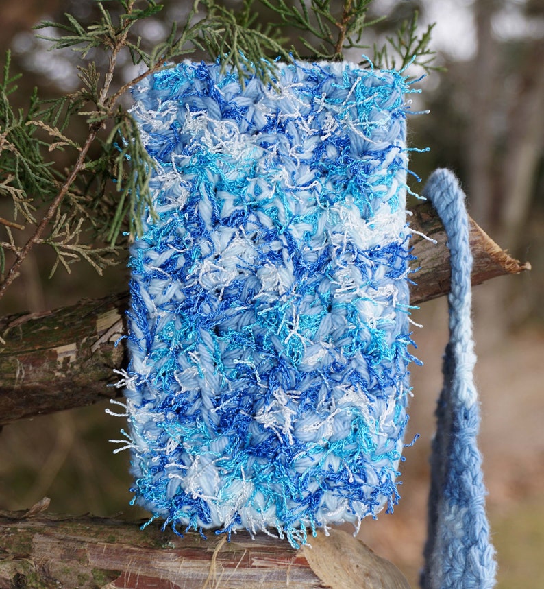 May include: A blue and white crocheted bag with a long blue strap. The bag has a fuzzy texture and is made with a variety of blue and white yarns.