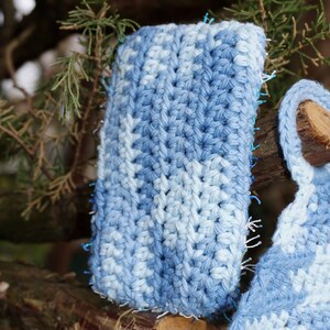May include: A close-up of a blue and white crocheted phone case with a textured pattern. The case is made with a soft yarn and has a fringed edge.