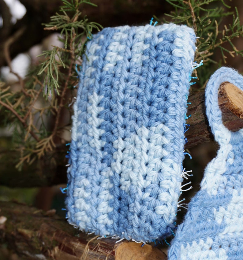 May include: A close-up of a blue and white crocheted phone case with a textured pattern. The case is made with a soft yarn and has a fringed edge.