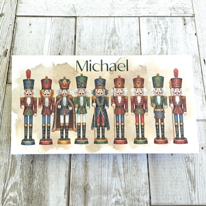 May include: A rectangular print featuring a collection of colorful nutcracker figures. Each nutcracker is dressed in a unique uniform with varying colors, including red, green, blue, and gold. The name "Michael" is printed above the figures.