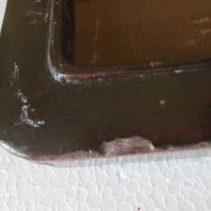 May include: A dark brown rectangular tray with a raised edge and a smooth, glossy finish. The surface shows visible signs of wear, including small scratches and chipped paint along the outer rim, revealing a lighter reddish-brown base layer.