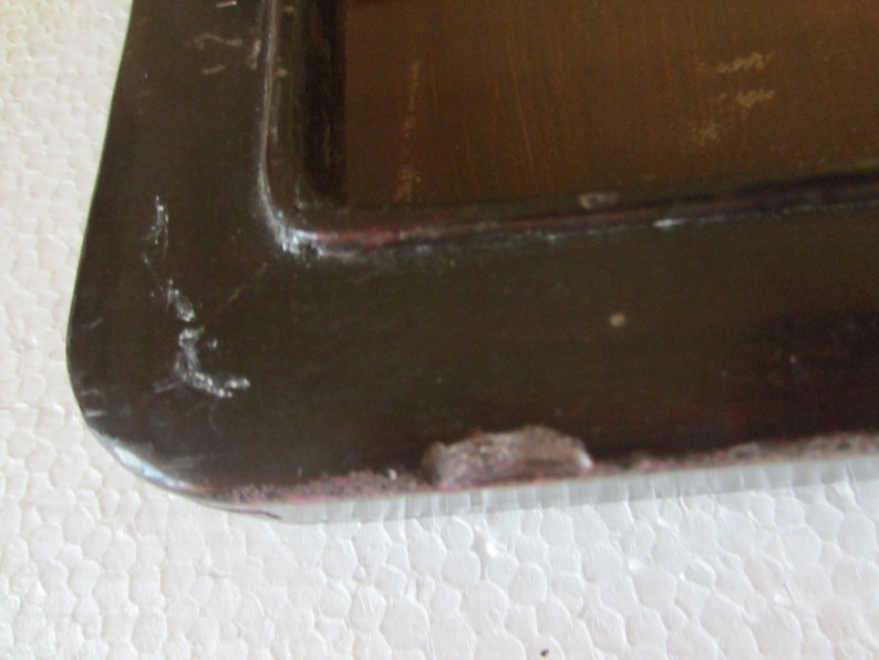 May include: A dark brown rectangular tray with a raised edge and a smooth, glossy finish. The surface shows visible signs of wear, including small scratches and chipped paint along the outer rim, revealing a lighter reddish-brown base layer.