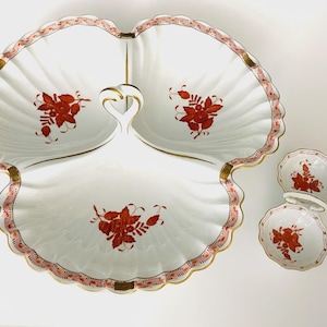May include: A white, three-section serving dish with a scalloped edge and a gold handle. The dish features red floral designs and a red and gold border. Two matching small bowls are also present.