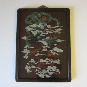 May include: A rectangular wall hanging featuring a dark brown background with a detailed illustration of a green phoenix and a red dragon intertwined among white stylized clouds. The artwork is encased in a dark brown frame with a metal hanger.