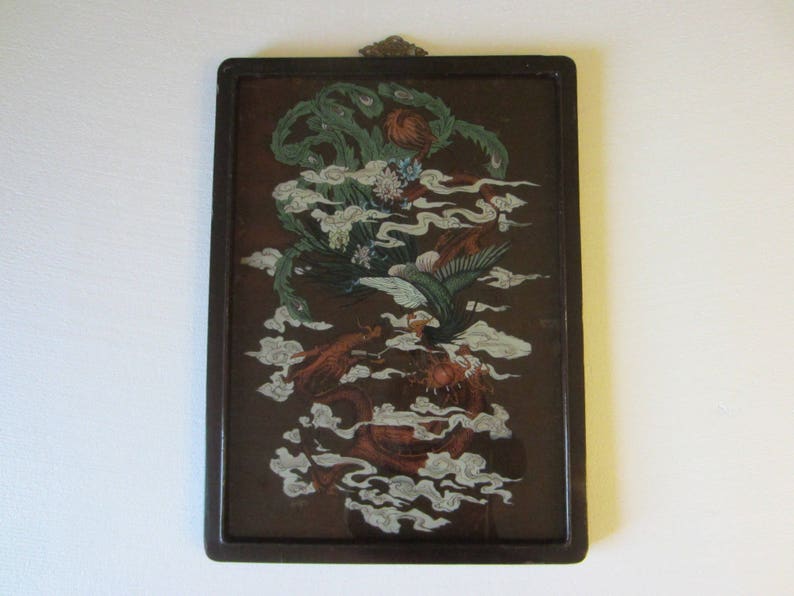 May include: A rectangular wall hanging featuring a dark brown background with a detailed illustration of a green phoenix and a red dragon intertwined among white stylized clouds. The artwork is encased in a dark brown frame with a metal hanger.
