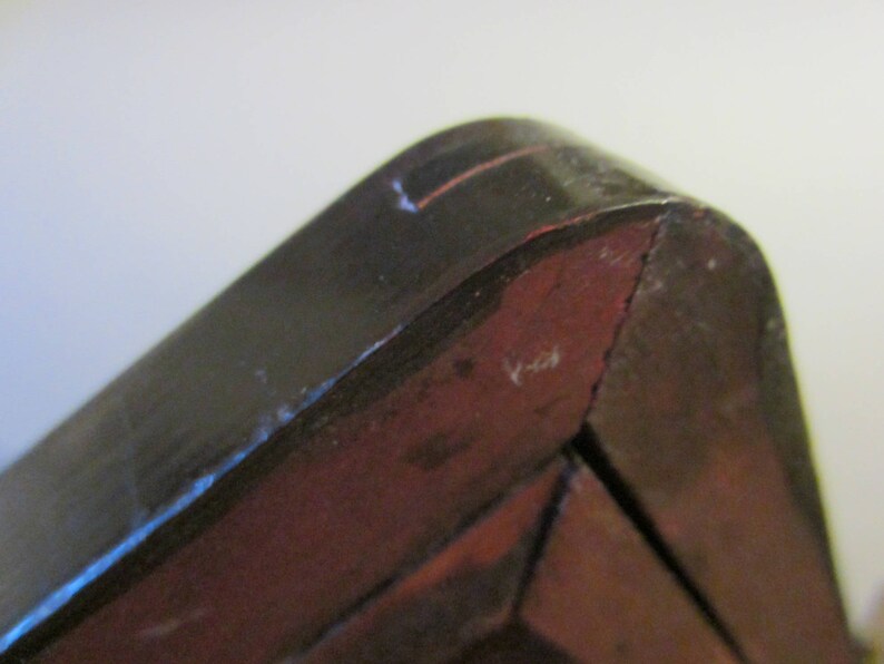 May include: A close-up view of a dark brown wooden corner joint with a smooth, polished finish. The structure features a curved edge meeting a flat side, revealing a reddish-brown interior tone where the wood grain is visible along the angled seam.