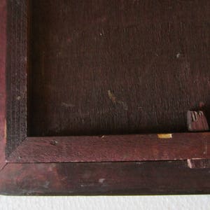 May include: A dark brown wooden frame with a mitered corner joint and a visible wooden peg fastener on the side. The frame features a deep, rich wood grain texture and a rectangular inner opening, showing signs of wear on the edges.