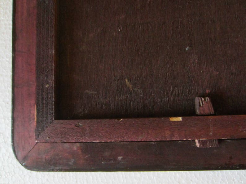 May include: A dark brown wooden frame with a mitered corner joint and a visible wooden peg fastener on the side. The frame features a deep, rich wood grain texture and a rectangular inner opening, showing signs of wear on the edges.