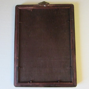 May include: A rectangular wooden picture frame shown from the back, featuring a dark brown finish, a flat backing board secured with small metal tabs, and a decorative brass-colored metal hanging bracket attached to the top center edge.