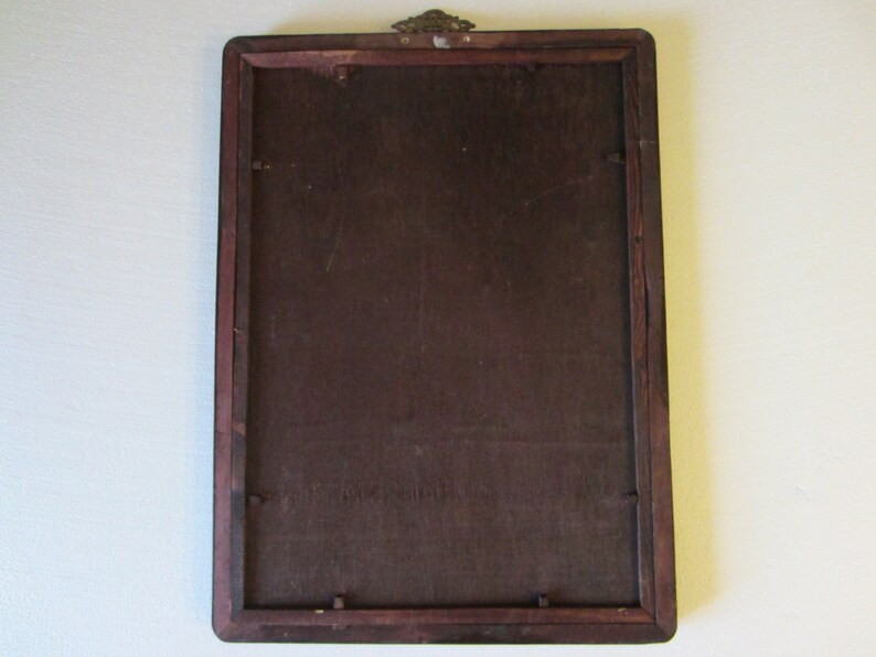 May include: A rectangular wooden picture frame shown from the back, featuring a dark brown finish, a flat backing board secured with small metal tabs, and a decorative brass-colored metal hanging bracket attached to the top center edge.