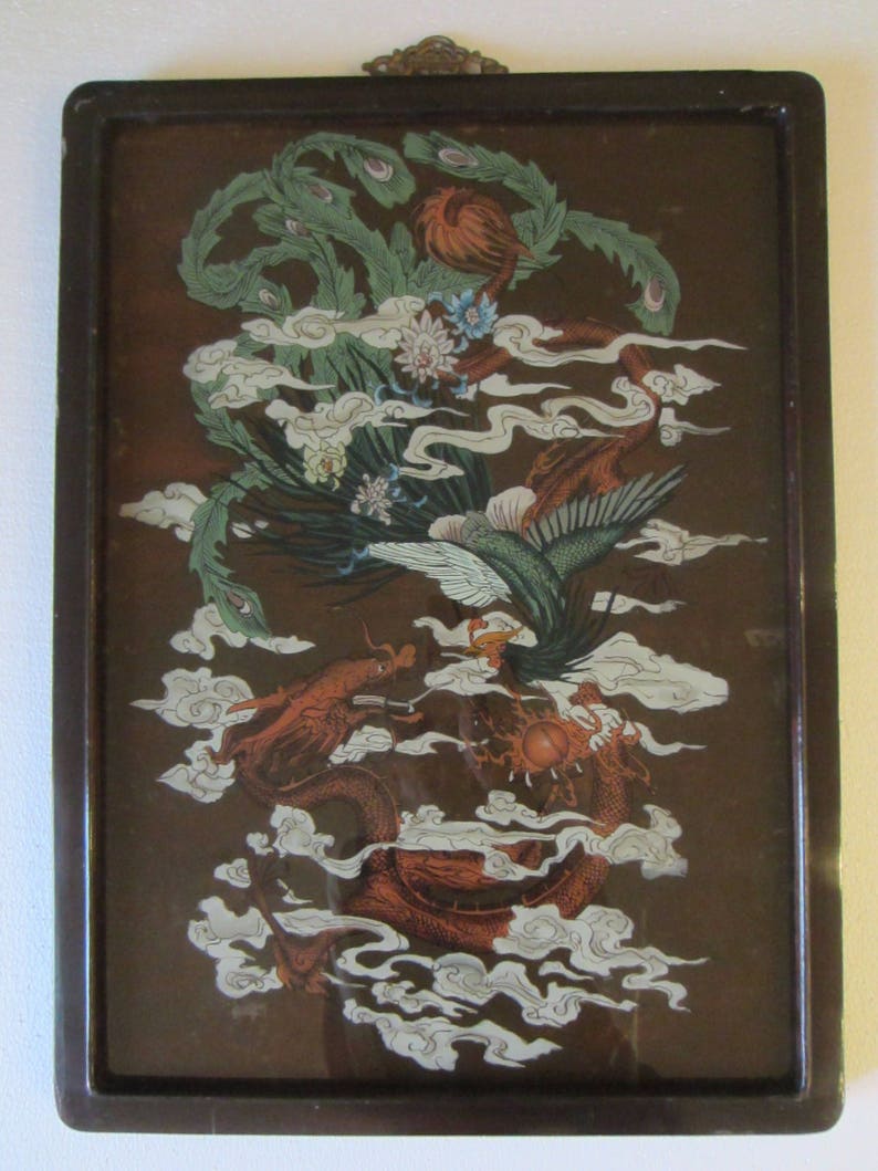 May include: A rectangular wall hanging featuring a dark brown background with a detailed illustration of a green phoenix and a red dragon intertwined among white stylized clouds. The artwork is encased in a dark brown frame with a metal hanger.