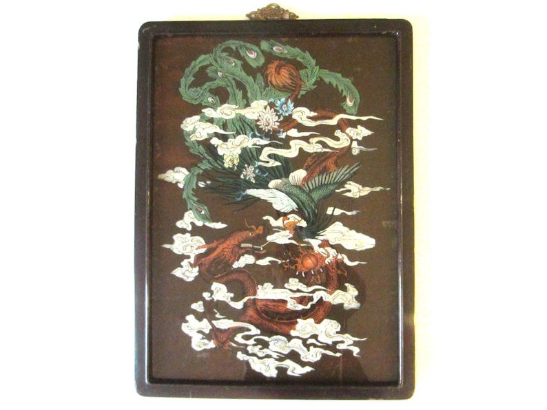 May include: A rectangular wall hanging featuring a dark brown frame and a central illustration of a green phoenix and a red dragon intertwined among white clouds. The artwork includes floral accents and a small decorative metal hanger at the top.