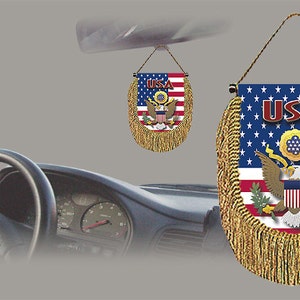 May include: A red, white, and blue American flag car charm with gold fringe and the word "USA" in red letters. The charm features the Great Seal of the United States, which includes an eagle with outstretched wings.