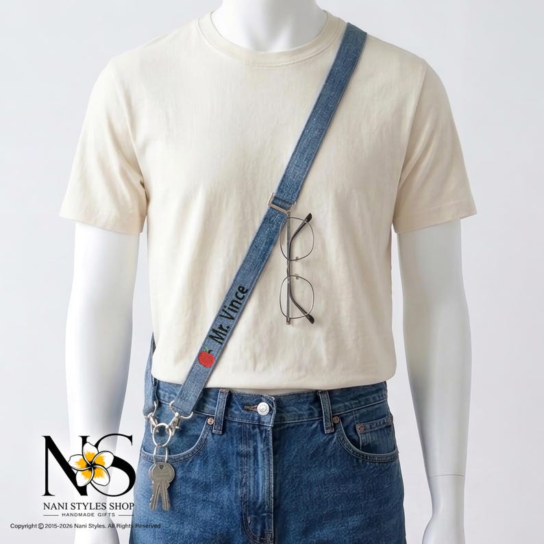 May include: A blue denim lanyard worn across the torso, featuring the embroidered text Mr. Vince and a small red apple icon. The strap includes a metal clip holding a set of silver keys and a pair of thin-rimmed glasses hanging from the fabric.