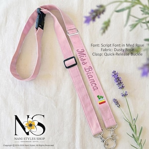 May include: A dusty rose fabric lanyard featuring a black quick-release buckle, an adjustable black slider, and two silver-toned metal lobster clasps. The strap is embroidered with the text Miss Bianca in a script font and a small cactus icon.