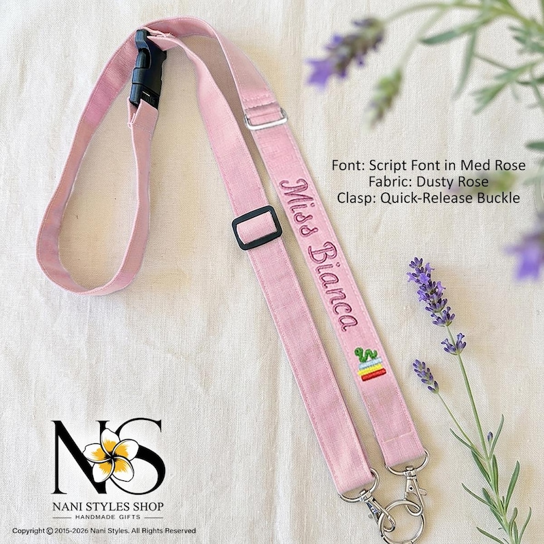 May include: A dusty rose fabric lanyard featuring a black quick-release buckle, an adjustable black slider, and two silver-toned metal lobster clasps. The strap is embroidered with the text Miss Bianca in a script font and a small cactus icon.