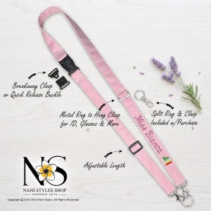 May include: A light pink fabric lanyard featuring an adjustable length slider, a black plastic breakaway clasp, and a metal ring for attachments. The strap is embroidered with the text Miss Bianca and a small rainbow icon, including a split ring and clasp.