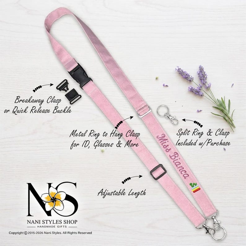 May include: A light pink fabric lanyard featuring an adjustable length slider, a black plastic breakaway clasp, and a metal ring for attachments. The strap is embroidered with the text Miss Bianca and a small rainbow icon, including a split ring and clasp.