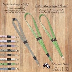 May include: Two different types of keychains, one with a triple breakaway feature and the other with a dual breakaway feature. The keychains are made of a woven fabric with a gradient color design. The keychains are available in a variety of colors, including berry, lilac, eggplant, olive, nutmeg, natural, palm, and slate blue. The keychains are shown on a wooden surface. The text "Triple breakaway (3 pts)" and "Dual breakaway Layard (2 pts)" is shown above the keychains. The text "Key Fob Options" is shown below the keychains. The text "Choose an optional detachable key Fob" is shown below the text "Key Fob Options".