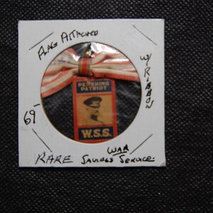 May include: A vintage pin featuring a red, white, and blue ribbon and a rectangular tag with a portrait and the text "Pershing Patriot W.S.S.". The pin is mounted on a white card with handwritten text.