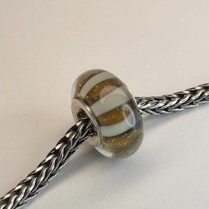 May include: A clear glass bead with white and gold stripes. The bead is on a silver chain.