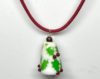Puede incluir: Collar con colgante de cristal en forma de campana. El colgante es blanco con diseños florales verdes y cuentas rojas. El collar tiene un cordón rojo.