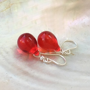 May include: A pair of red glass teardrop earrings with silver wire hooks.