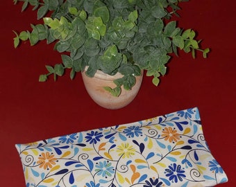 May include: A rectangular fabric pillow featuring a white background with a repeating pattern of blue, yellow, and orange flowers, thin dark blue stems, and small leaves. The pillow is positioned below a small green potted plant.