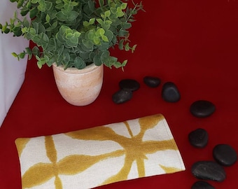 May include: A rectangular fabric eye pillow featuring a mustard yellow and off-white abstract geometric pattern. The pillow has a flat, elongated shape with visible stitching along the edges, showcasing a textured textile surface.