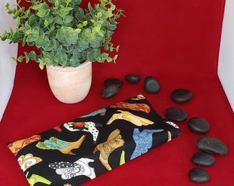 May include: A rectangular fabric pouch featuring a black background with a repeating pattern of various colorful boots in shades of yellow, blue, white, and orange. The pouch is positioned on a red surface next to several smooth black stones.