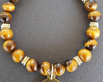 May include: A beaded bracelet featuring polished brown and gold tiger's eye gemstone beads interspersed with small gold-toned metal spacers. A round gold-toned metal charm hangs from the center, engraved with the text I am strong.