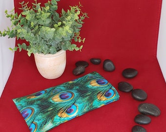 May include: A rectangular fabric eye pillow featuring a vibrant peacock feather pattern in shades of teal, emerald green, gold, and deep blue. The fabric has a detailed print of multiple eye-shaped feather motifs across the entire surface.