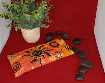 May include: A rectangular fabric pouch featuring a vibrant orange and yellow tie-dye background with black printed sun, star, and spiral motifs. The pouch is positioned horizontally, showcasing a repeating celestial pattern across its surface.