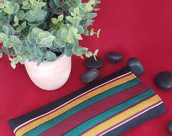 May include: A rectangular fabric pouch featuring a pattern of vertical stripes in yellow, teal, and maroon, separated by thin white lines on a black background. The fabric has a textured, woven appearance with a consistent repeating design.