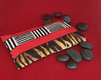 May include: A rectangular fabric pouch featuring a vibrant red section with black and white geometric stripes, contrasted by a section with a black and brown tiger-like animal print pattern. The pouch is surrounded by several smooth black stones.