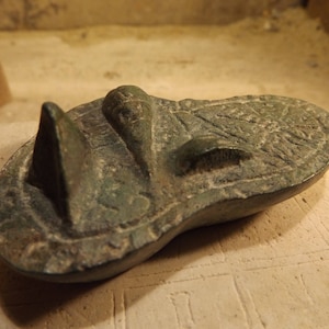 May include: A green bronze artifact with intricate carvings and a pointed shape. The artifact is likely an ancient object with historical significance.