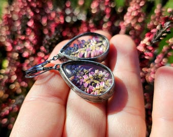 May include: A pair of silver teardrop earrings with dried pink and purple flowers encased in clear resin.