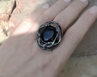 May include: A silver ring with a black gemstone set in a swirling, organic design.