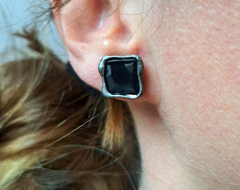 May include: A pair of silver square earrings with black square stones in the center.