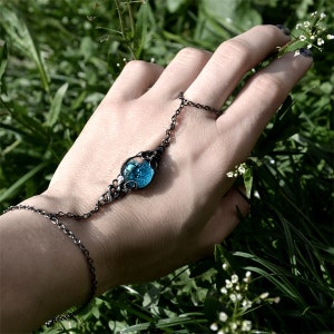 May include: A black chain bracelet with a blue glass orb pendant. The orb is surrounded by a delicate metal design.
