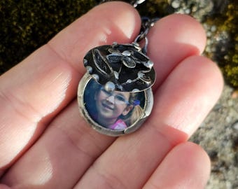 May include: A silver locket necklace with a floral design on the lid. The locket is open, revealing a photo of a young girl.