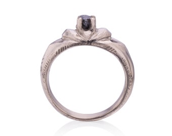Könnte beinhalten: Ein silberner Ring mit einer strukturierten Band und einem einzigen schwarzen Diamanten in der Mitte.